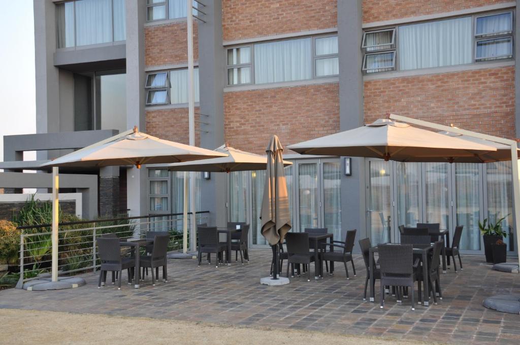 un patio con mesas y sombrillas frente a un edificio en Merchant Business Class Hotel en Henley on Klip