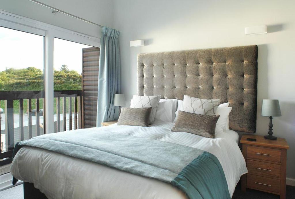 a bedroom with a large bed with a large window at Harlyn lodge Hot Tub Lodge at Retallack Resort in Saint Columb Major
