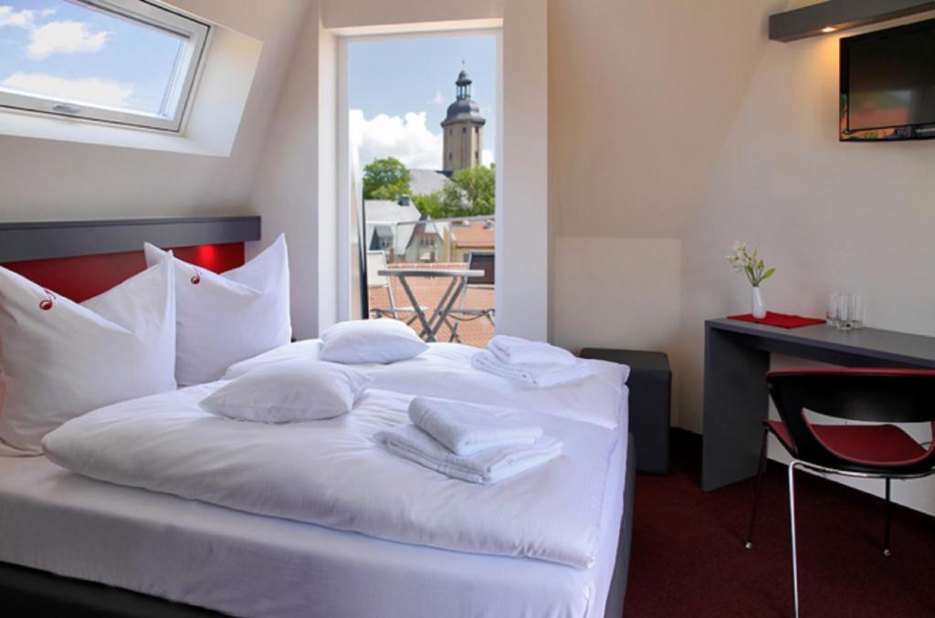 een slaapkamer met een bed met witte lakens en kussens bij Hotel VielHarmonie in Jena