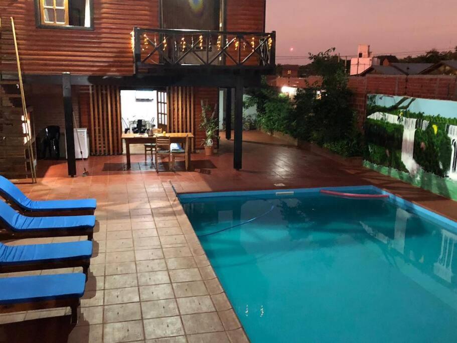 a swimming pool with chairs and a house at Hermosa y confortable cabaña in Puerto Iguazú