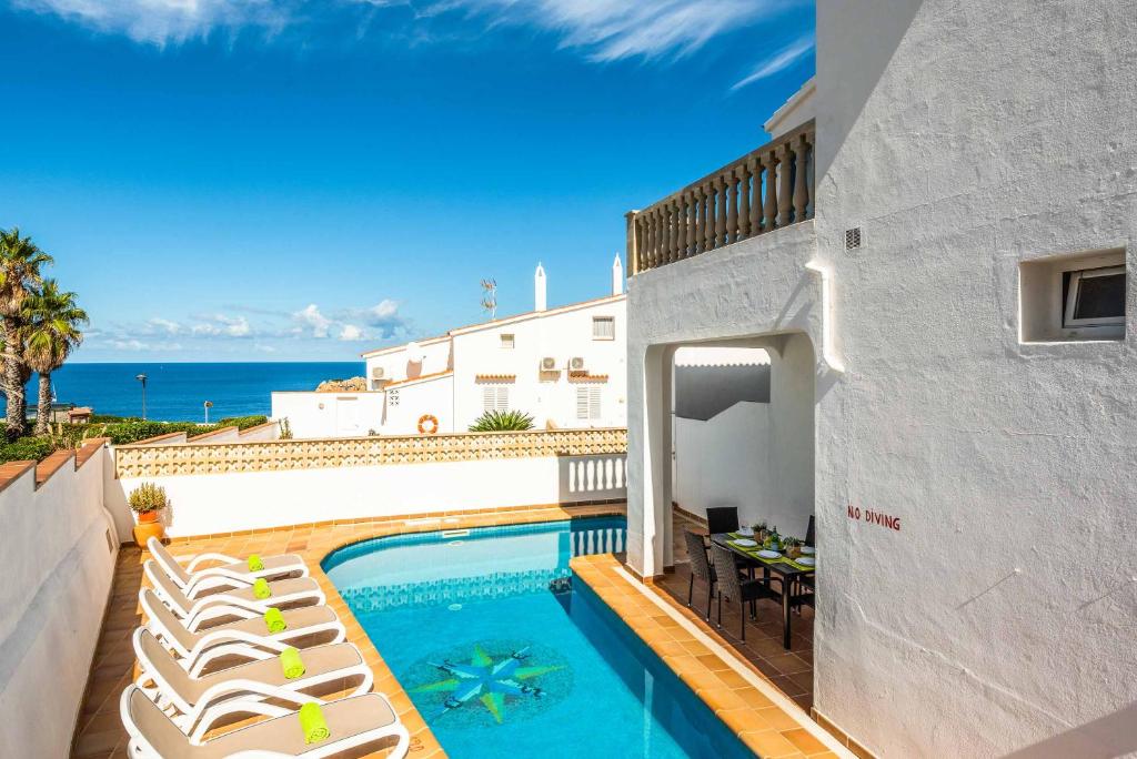 a swimming pool with lounge chairs and the ocean at Sa Luna in Arenal d'en Castell