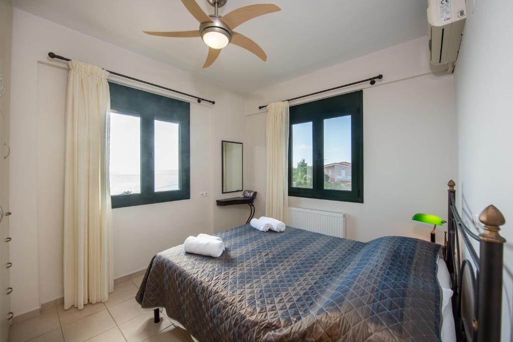 a bedroom with a bed with a ceiling fan and windows at Portela Apartments Kampoula in Keratokampos