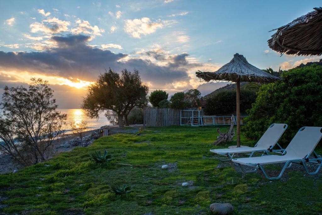 two chairs and an umbrella and the ocean at sunset at Portela Apartments Kampoula in Keratokampos