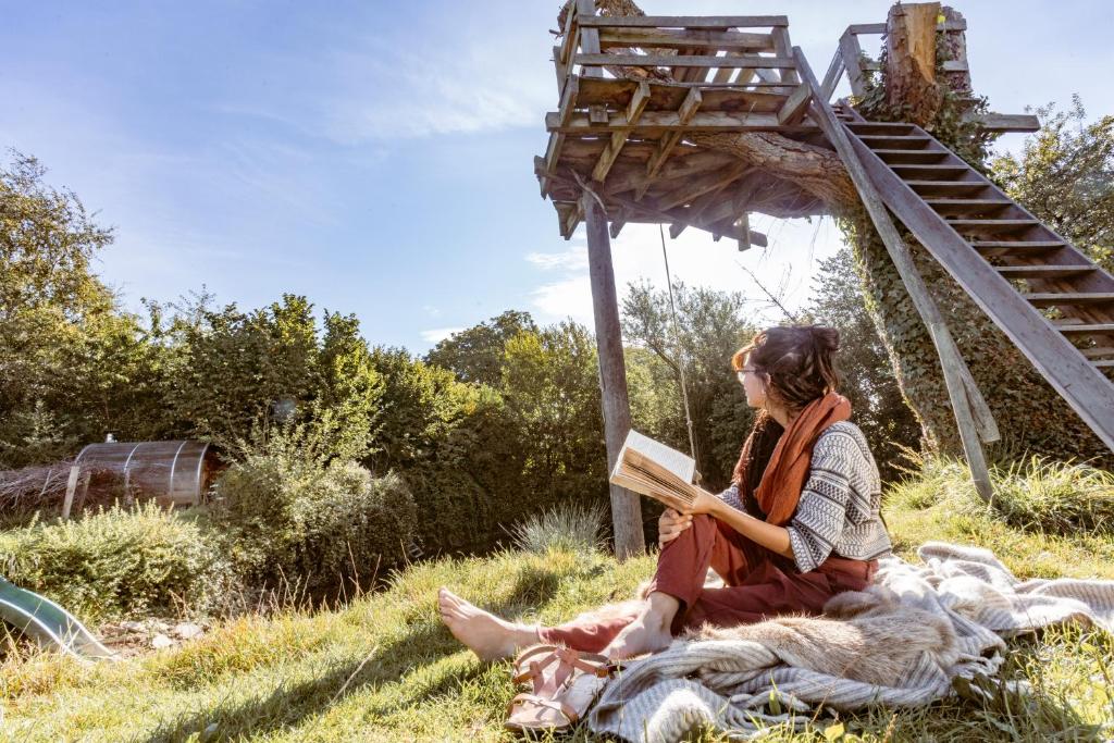 una mujer sentada en la hierba leyendo un libro en Vakantiewoning met sauna & hottub en zwempoel op Natuurterrein en Heuvelland
