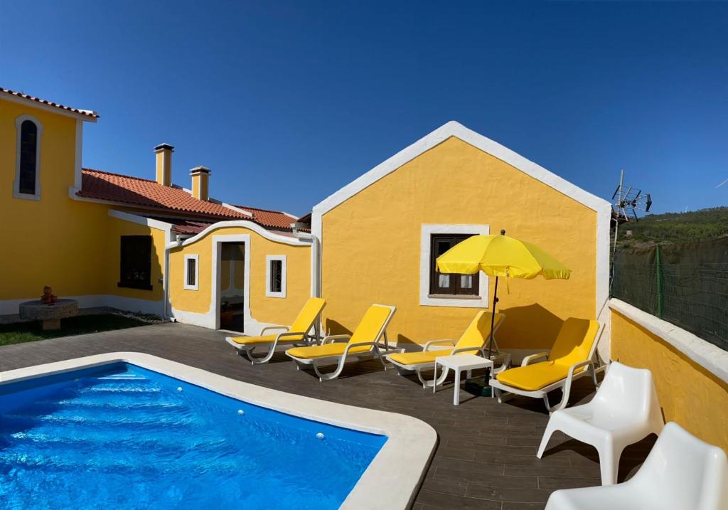 a pool with chairs and an umbrella next to a house at Casinhas dos Valados in Atouguia da Baleia