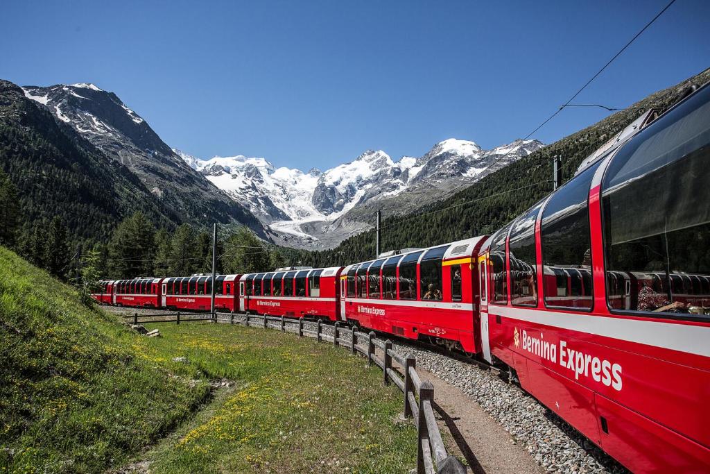 Ein roter Zug fährt die Gleise hinunter in die Berge in der Unterkunft Casa Lalla affittasi nel centro di Poschiavo in Poschiavo