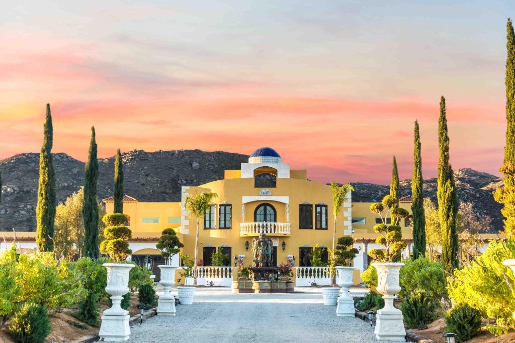 una grande casa gialla con una recinzione bianca e alberi di Palazzo del Valle, Alojamiento y Desayuno a Valle de Guadalupe