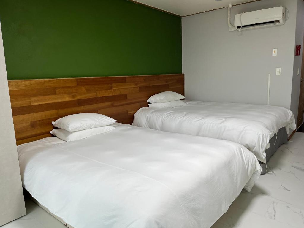 two white beds in a room with a green wall at Hill Hotel in Jeju