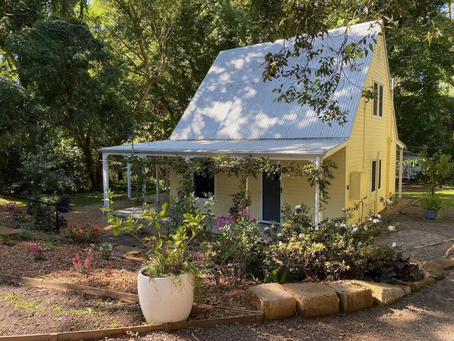 a yellow house with a blue roof and some flowers at Puddleduck Cottage at Maleny in Balmoral Ridge