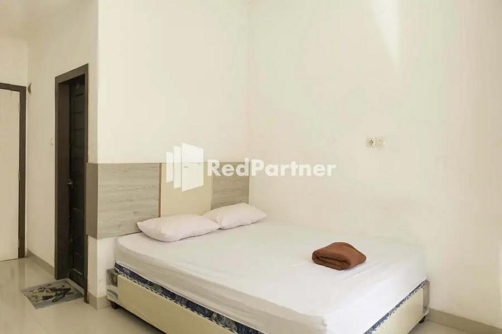 ein weißes Zimmer mit einem Bett mit zwei Kissen in der Unterkunft Radja Homestay Mitra RedDoorz in Pipulu