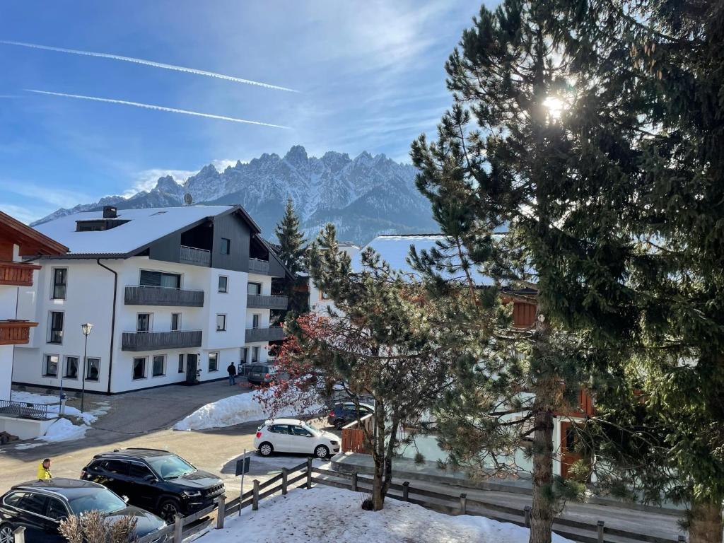 a building with cars parked in a parking lot with mountains at Appartamento a Dobbiaco nel cuore delle Dolomiti in Dobbiaco