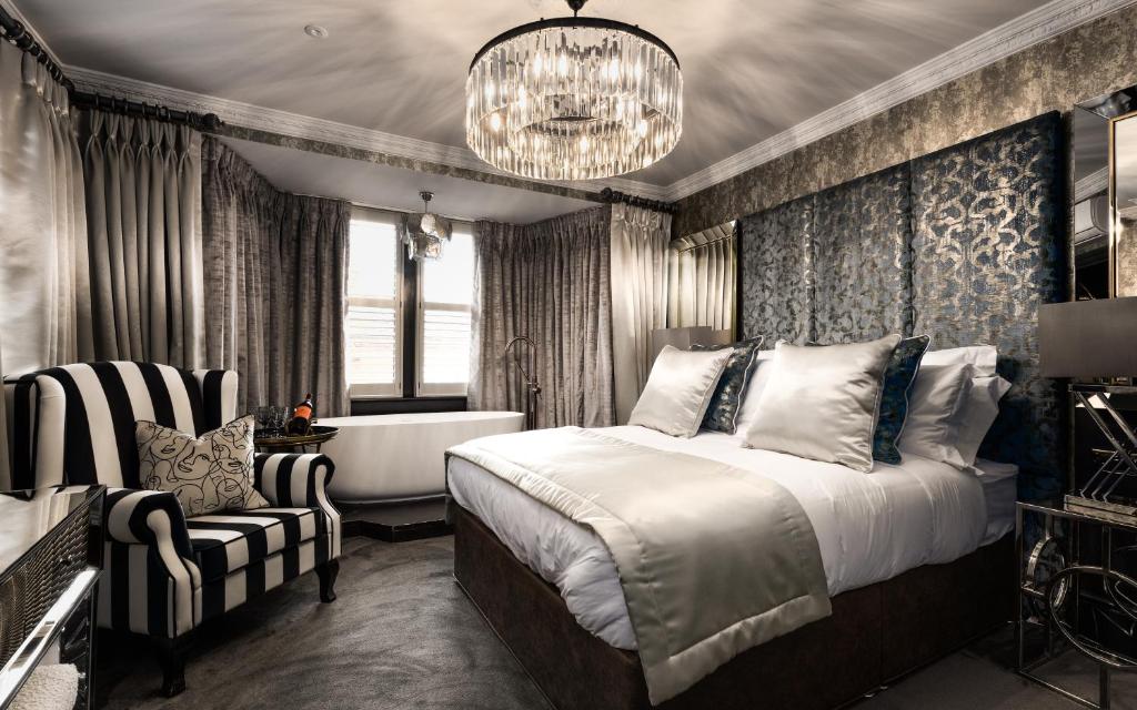 Schlafzimmer mit einem Bett, einer Badewanne und einem Kronleuchter in der Unterkunft Funky Monk Hotel in Epping