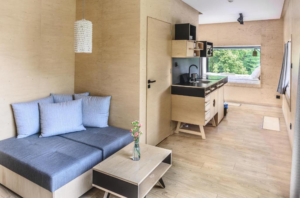 Minimal wood-paneled living space with gray sofa, small kitchenette, window seat and natural light.