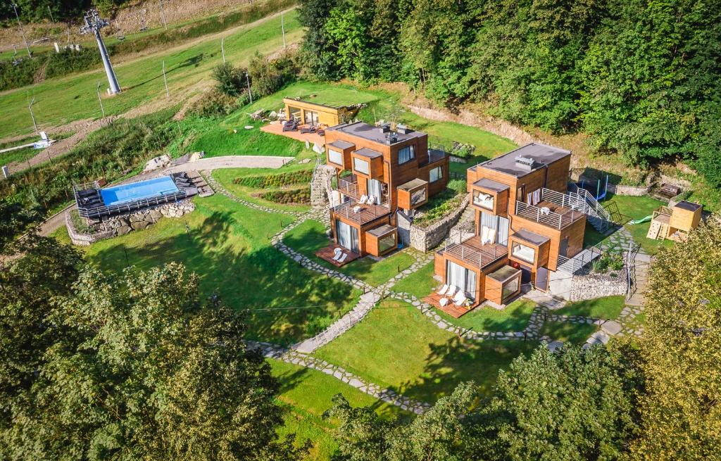 Aerial daytime view of modular wooden cabins set on green grounds with a pool, paths and trees.