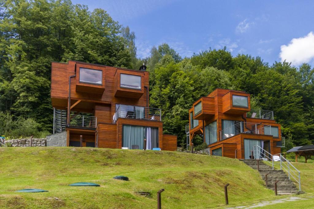 Cluster of modern wooden cube cabins on grassy slope with forest backdrop under blue sky.