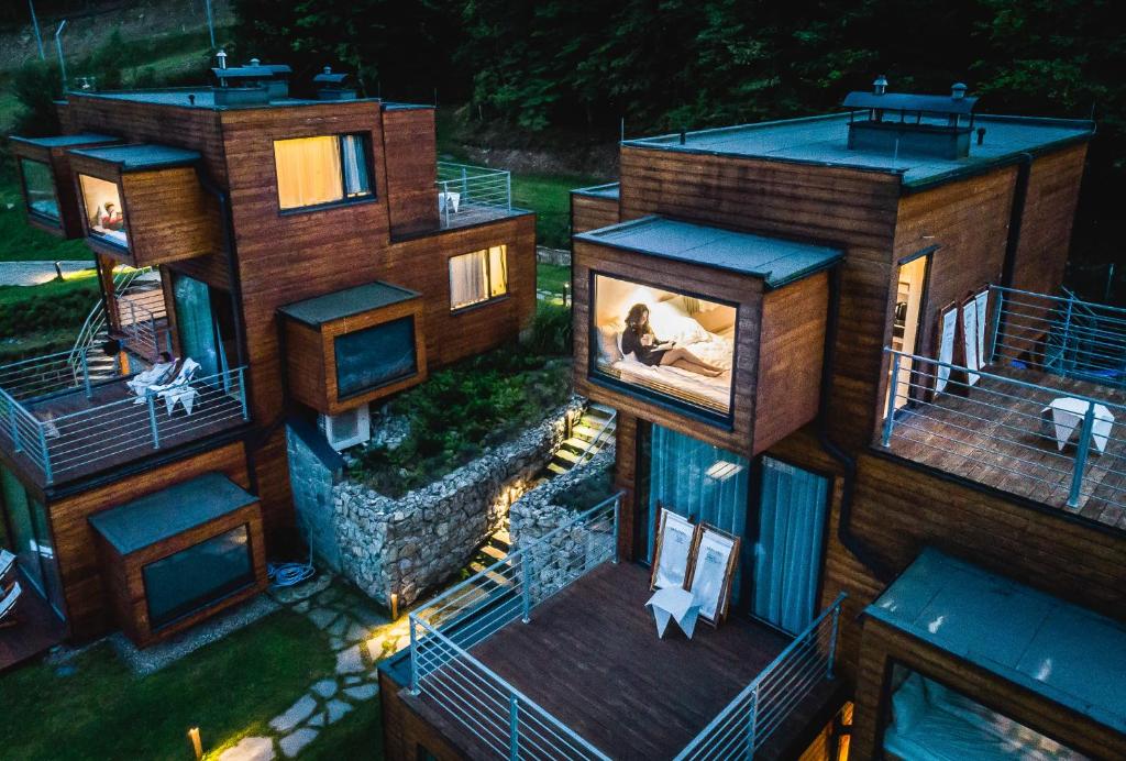 Night aerial of clustered wooden cabins with glowing windows, terraces and warm, inviting exterior lighting.