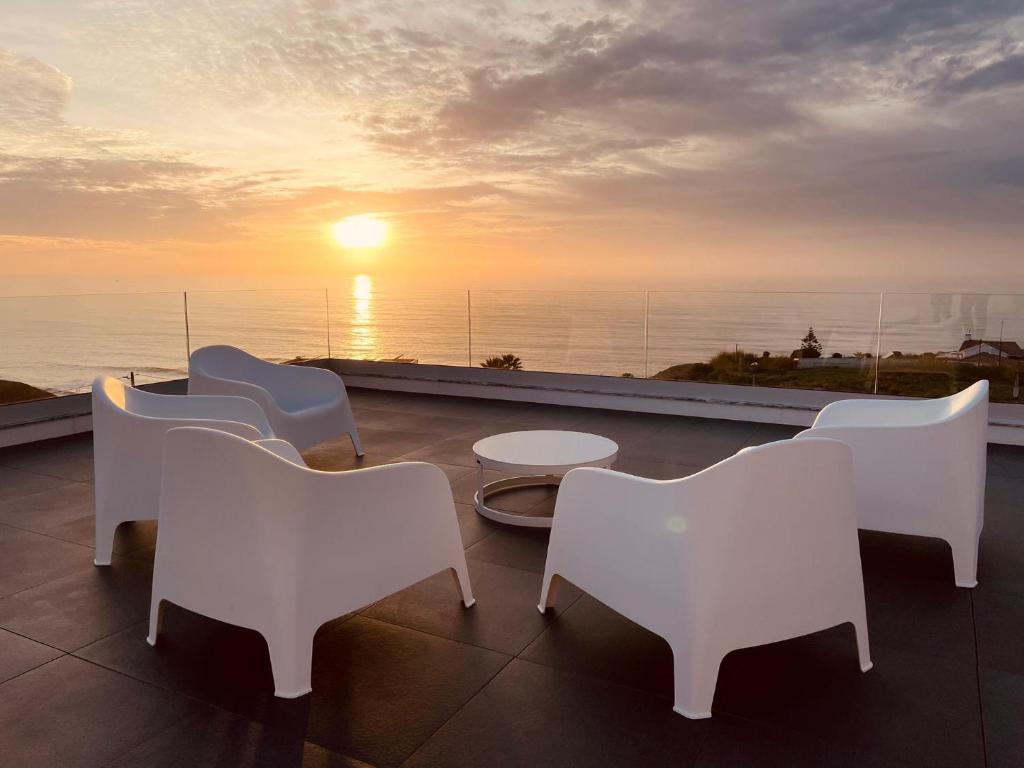 un grupo de sillas y mesas en un balcón con vistas a la puesta de sol en Villa Carpe Diem, en Lourinhã