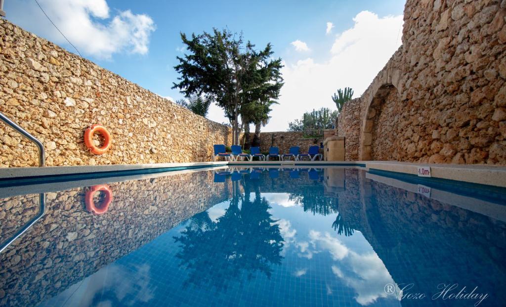 a swimming pool with chairs next to a stone wall at Ta' Salvu Holiday Home in Xagħra