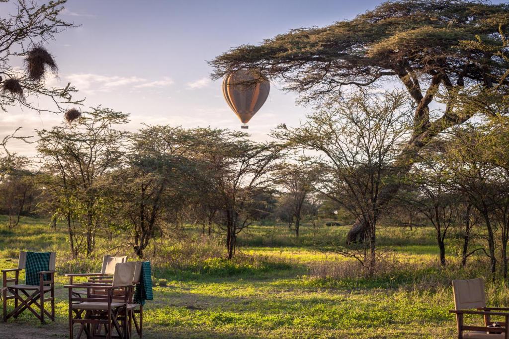 a hot air balloon flying over a field with chairs at Gnu Ndutu Camp in Sinoni