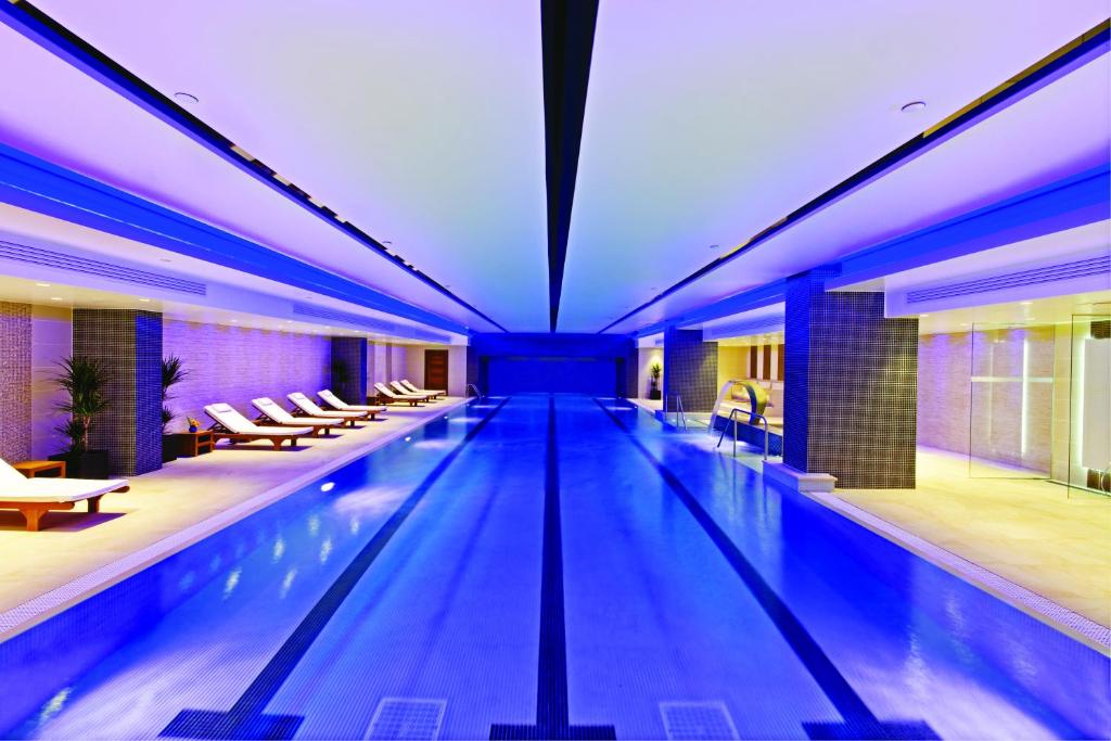 a large swimming pool in a hotel with blue lighting at Leonardo Royal London Tower Bridge in London