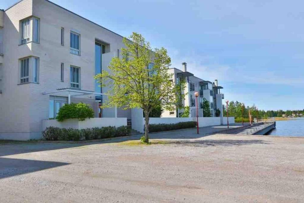 a building with a tree next to a body of water at Spacious Apartment close to the sea with 2 patios in Pietarsaari