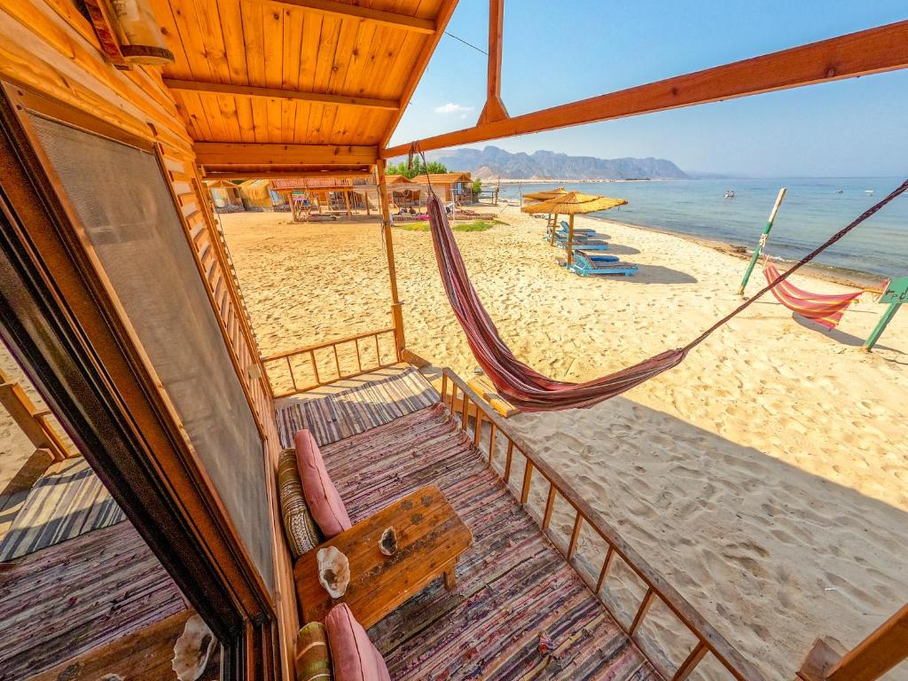 Habitación con vistas a una playa con sillas y hamaca. en Baraka Camp en Taba