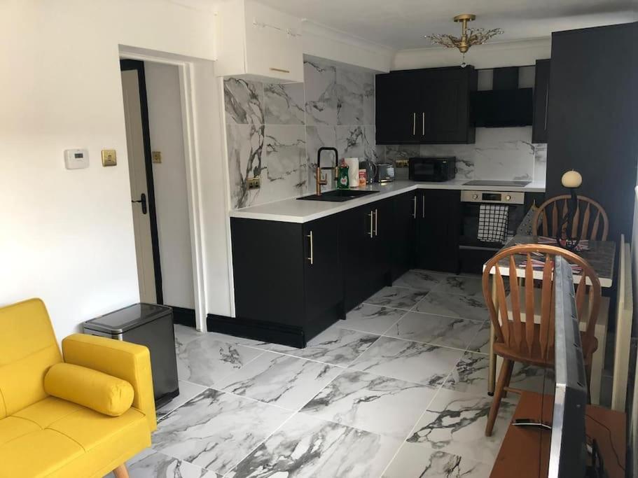 a kitchen with black cabinets and a yellow couch at Stylish and Modern Apartment close to Dover Port! in Kent