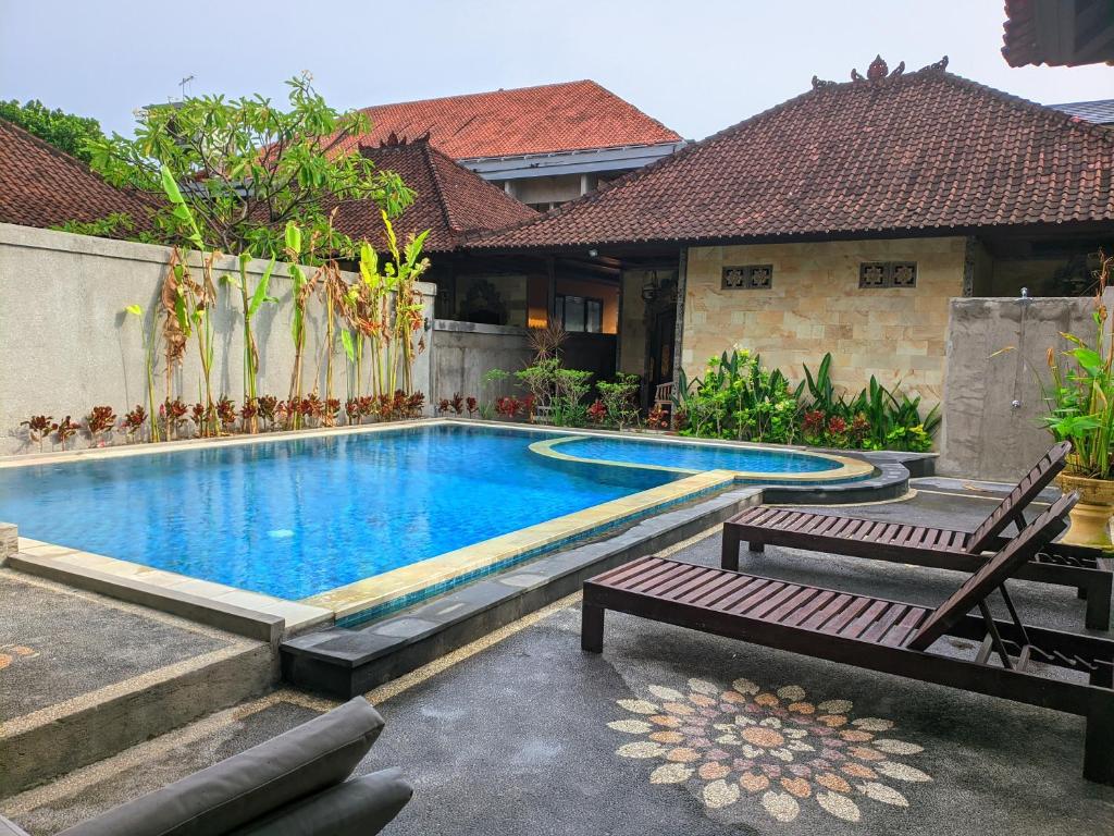 a swimming pool with two benches and a house at Taman Sari Cottages in Kuta