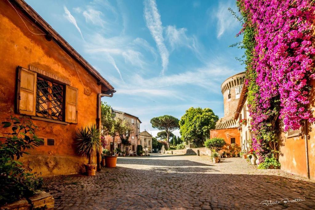 uma rua de calçada numa cidade velha com flores roxas em Casetta 46 em Ostia Antica
