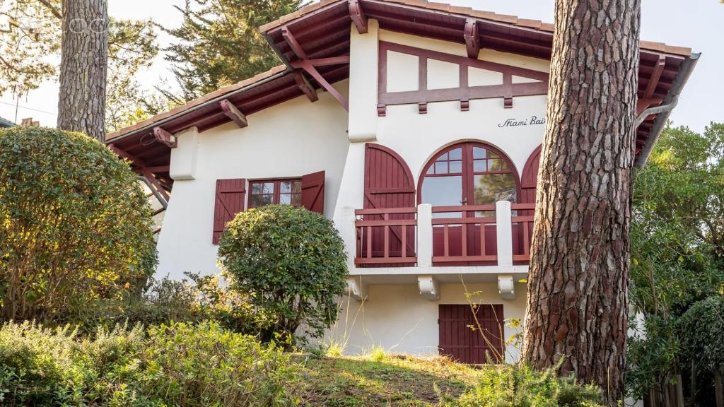 una casa blanca con ventanas rojas y un árbol en VILLA BAÏTA - Maison avec jardin proche de la Dune du Pyla, en La Teste-de-Buch