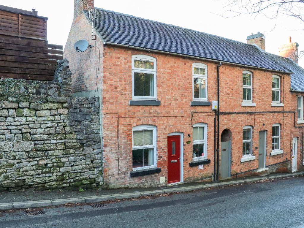 a brick building with a red door on a street at Poppy Cottage in Ashbourne