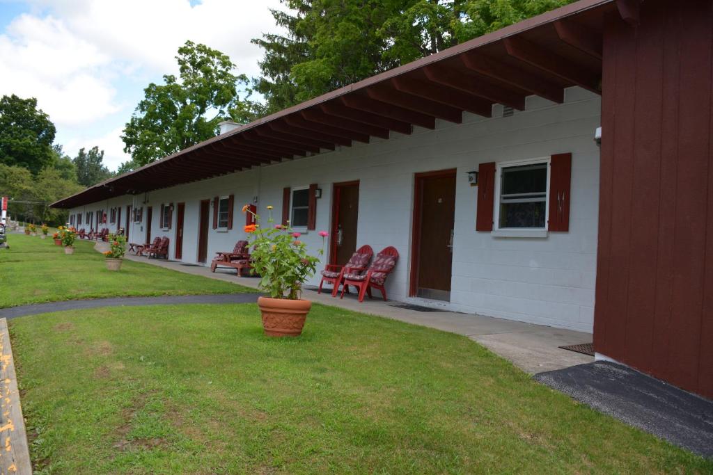 a white building with red chairs and a porch at The Village Motel in Richfield Springs