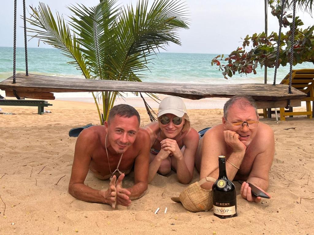 three people laying on the beach with a bottle of wine at Frangipani Beach Villa in Tangalle