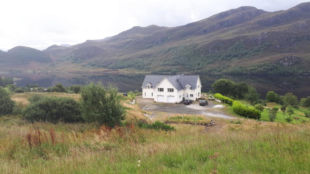 a white house on a hill with mountains in the background at Bunloyne in Sallachy