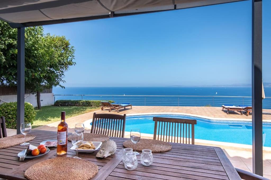 uma mesa de madeira com comida e copos de vinho e uma piscina em Amazing sea views Villa Voramar with pool em Llucmajor