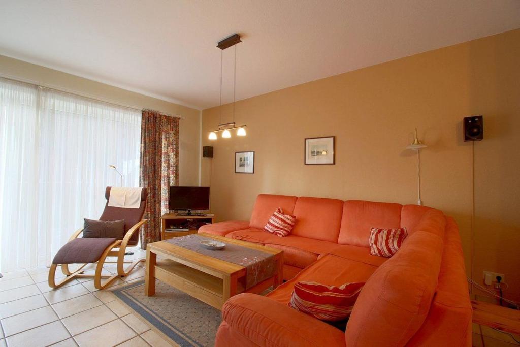 ein Wohnzimmer mit einem orangenen Sofa und einem Tisch in der Unterkunft DW10a FeWo Diekkieker in Spieka-Neufeld