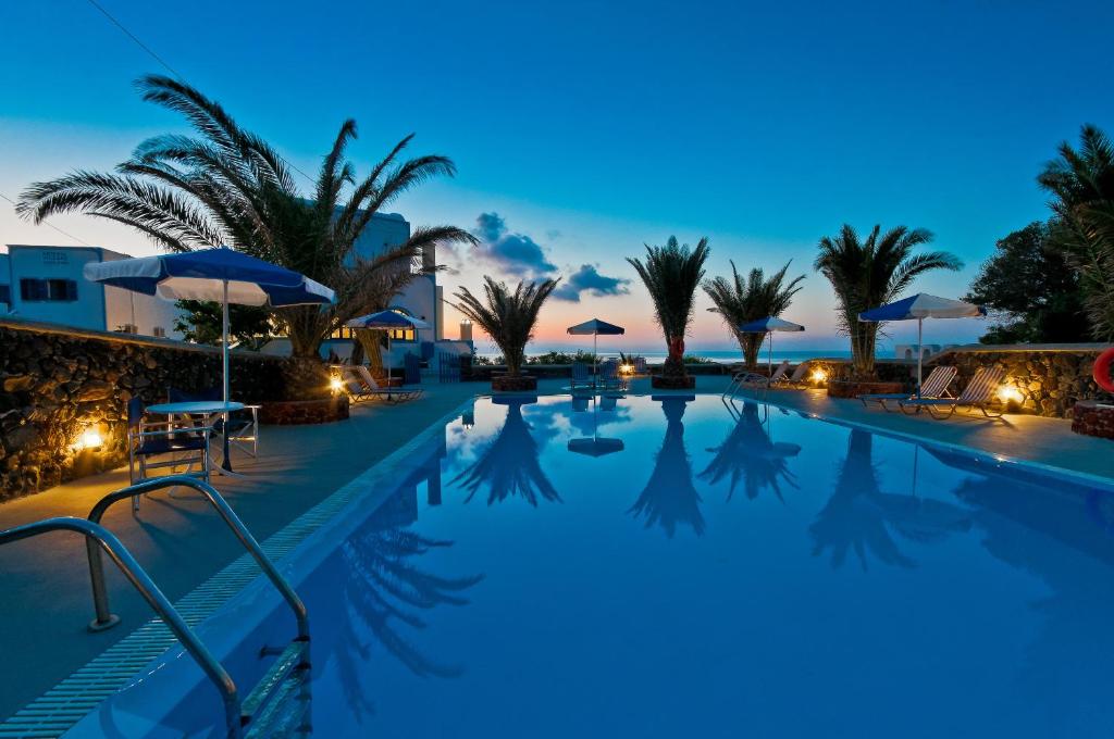 a pool at night with palm trees and umbrellas at Artemis Village in Karterados