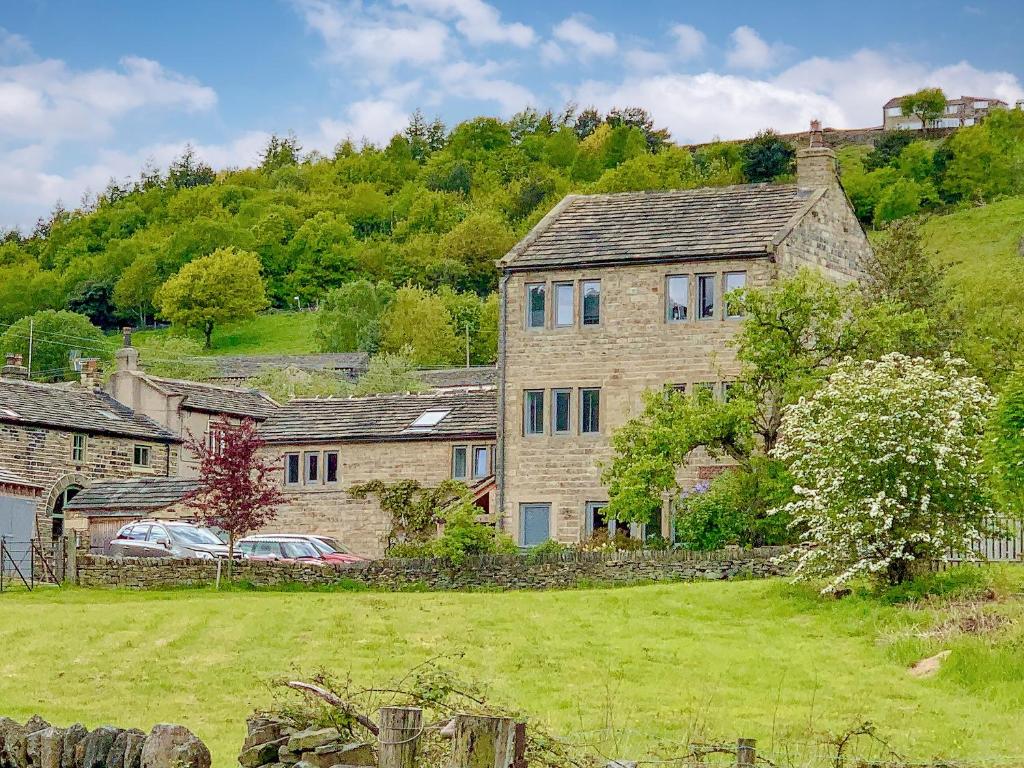 a large stone house on a hill with a yard at Weavers Cottage in Marsden