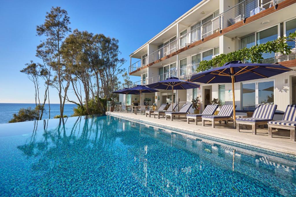 a swimming pool with chairs and umbrellas next to a building at Bannisters by the Sea Mollymook in Mollymook