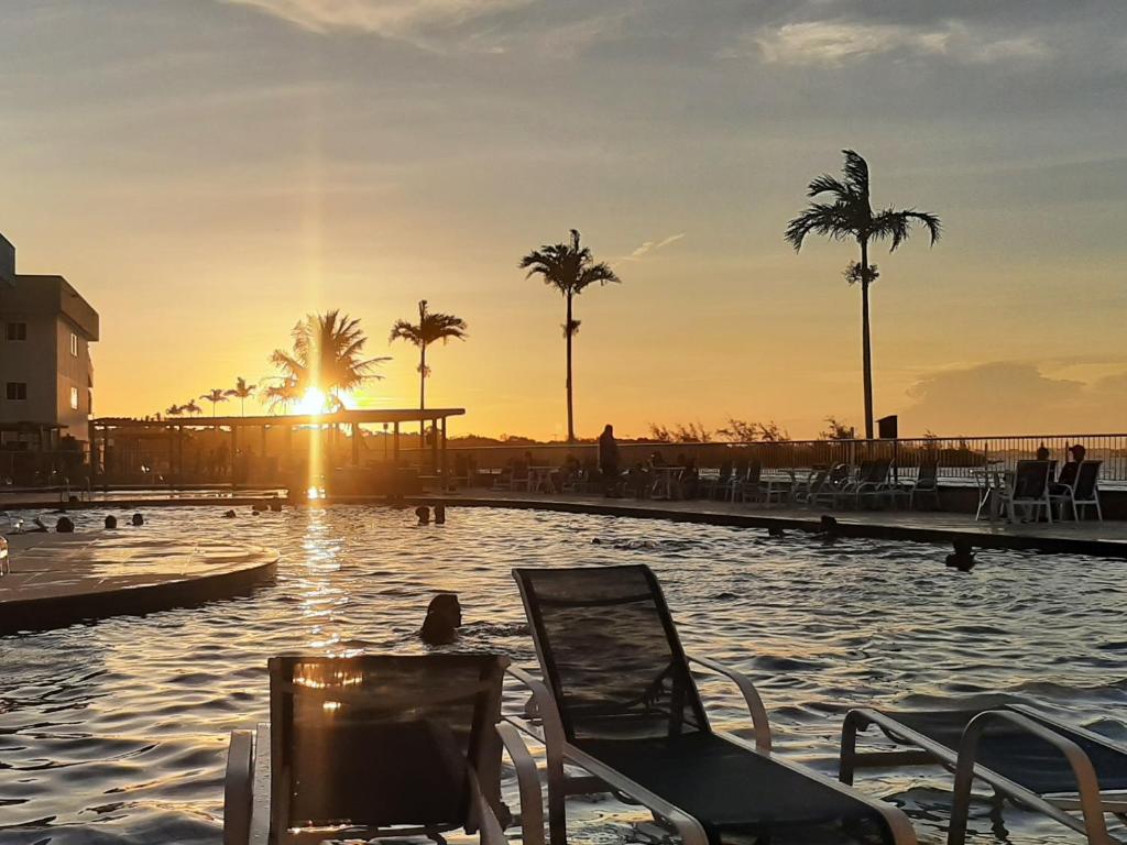 una piscina con una silla y palmeras al atardecer en Golden Lake - Arraial do Cabo, en Arraial do Cabo