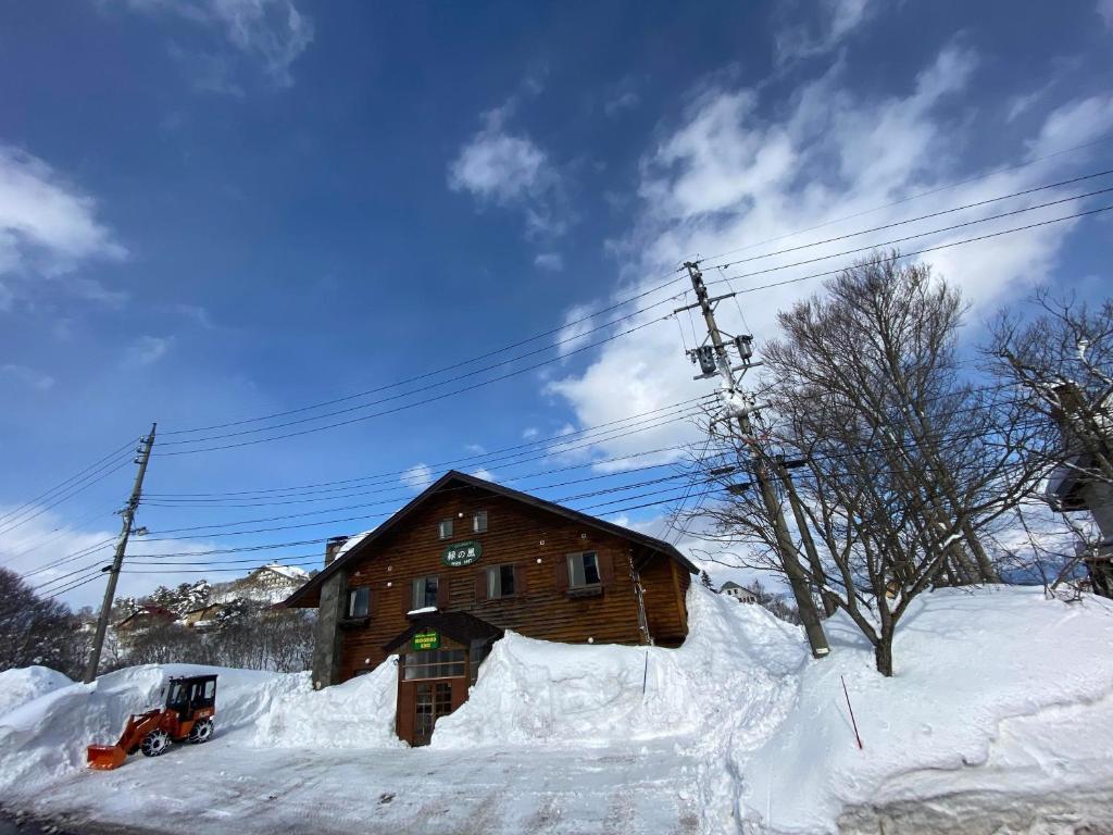 uma cabana de madeira na neve com uma mota de neve à frente em White Rabbit Madarao em Iiyama