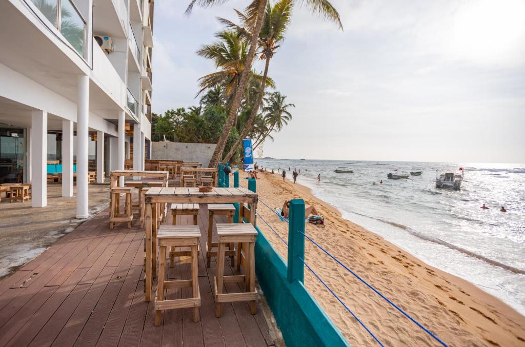 una playa con mesas y sillas y el océano en Hikkaduwa Beach Hotel en Hikkaduwa