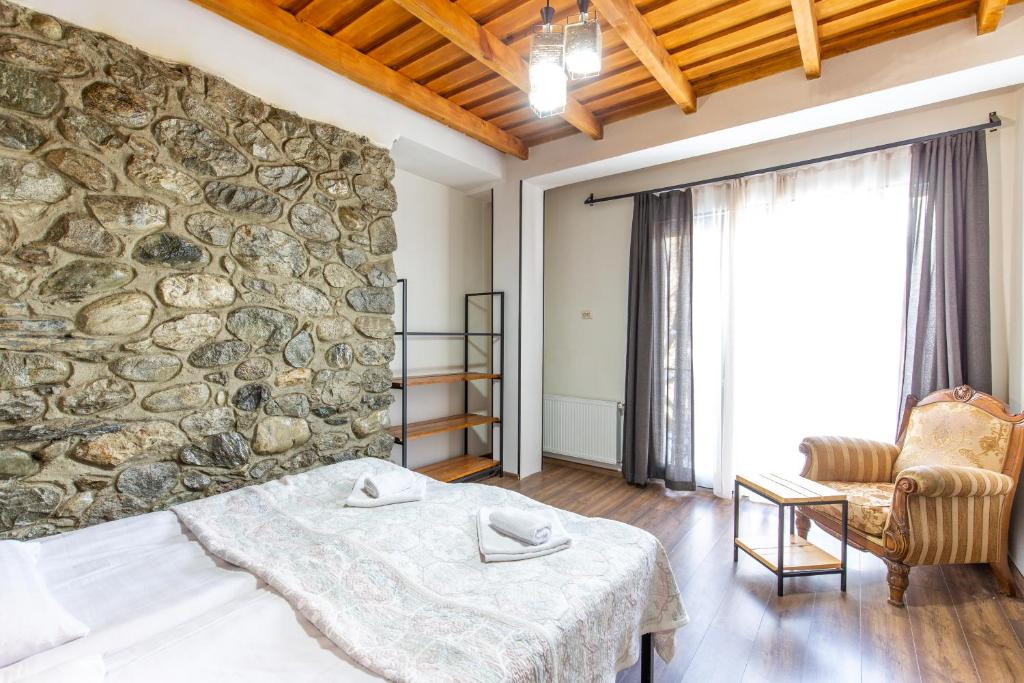 1 dormitorio con pared de piedra, cama y silla en Mestia Hotel Amirani en Mestia