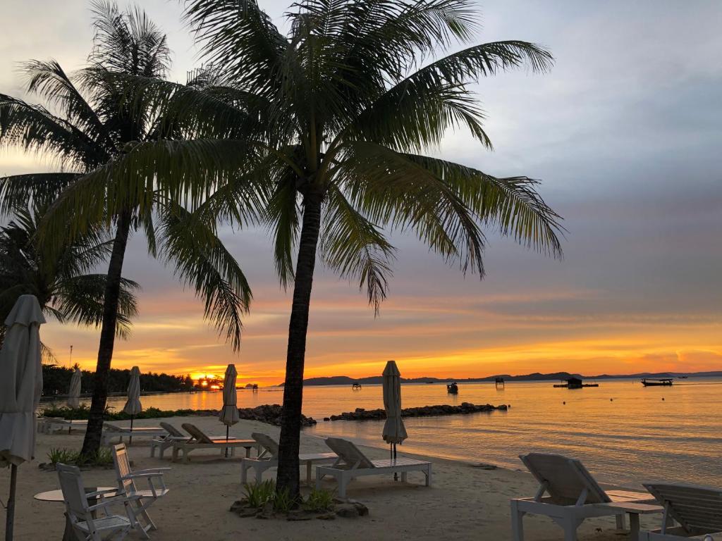 a beach with chairs and a palm tree at sunset at Gold Coast Phu Quoc Beach Resort in Phu Quoc