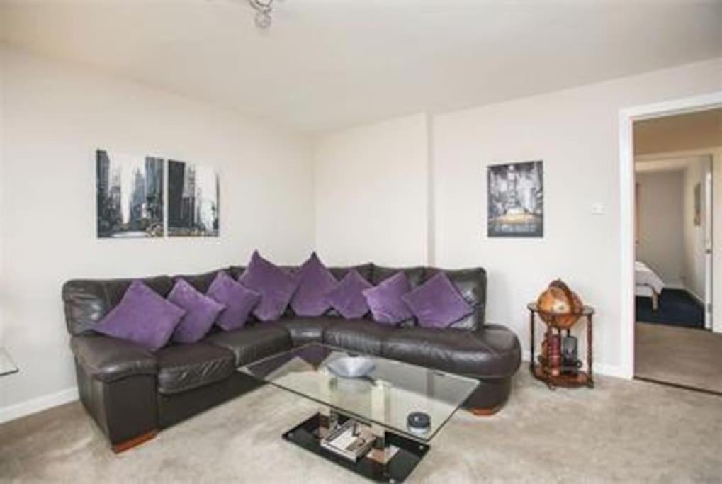 a living room with a black leather couch with purple pillows at Immaculate cosy flat next to Holyrood Park! in Edinburgh