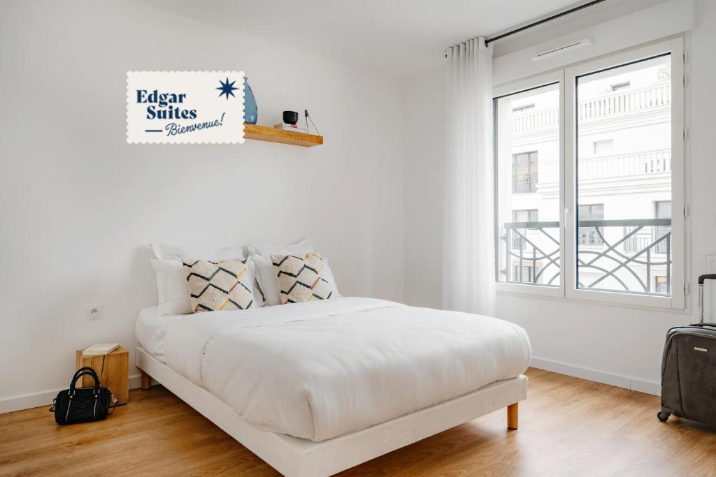 a white bedroom with a bed and a window at Edgar Suites Levallois – Jules Verne in Levallois-Perret