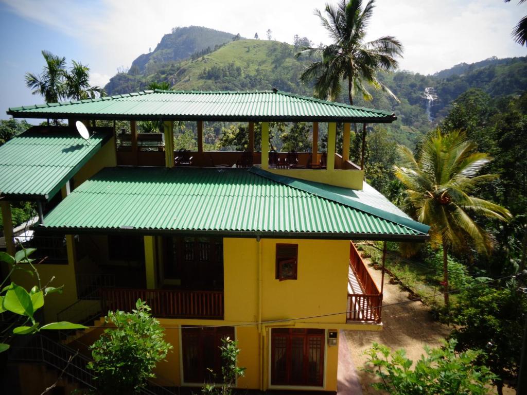 a yellow house with a green roof with a mountain in the background at Brilliant View Home Stay in Ella