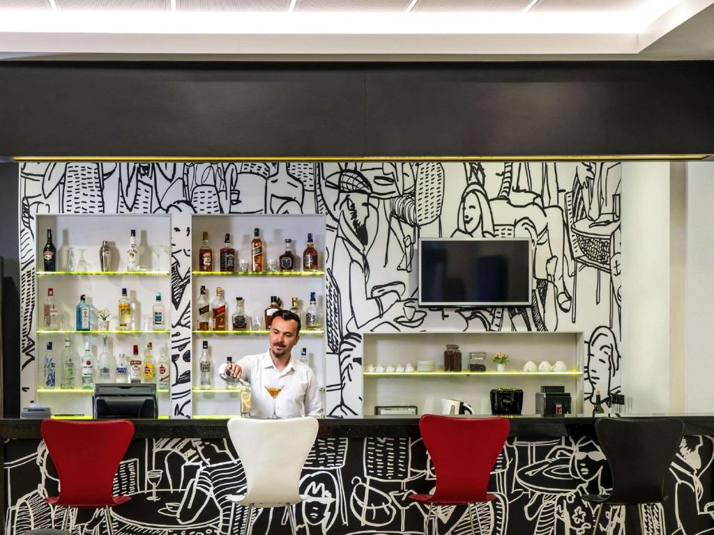 a man standing behind a counter in a room with red chairs at ibis Ankara Airport Hotel in Ankara