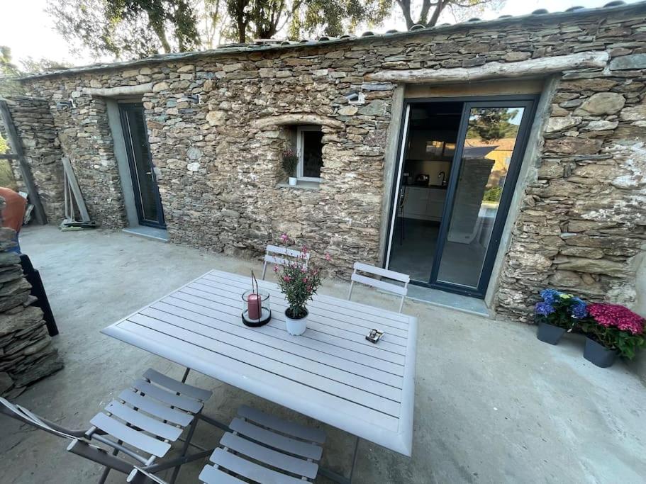 einem weißen Picknicktisch mit 2 Stühlen und einem Steingebäude in der Unterkunft Charmant logement in Rogliano