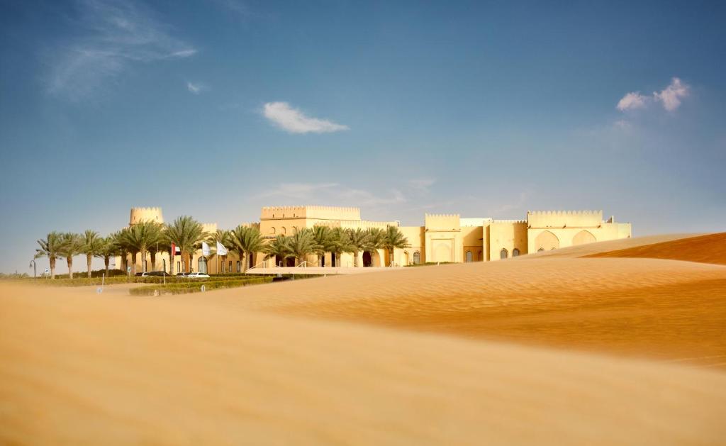 a view of a desert with a building and palm trees at Tilal Liwa Desert Retreat in Madīnat Zāyid